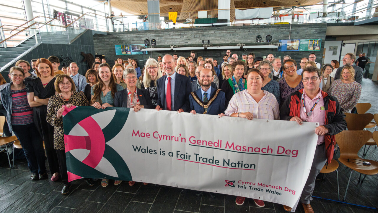 Photo of attendees at the Fair Trade Nation celebration event, standing behind a banner which reads "Wales is a Fair Trade Nation".